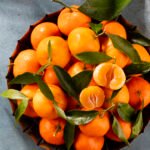 Fresh mandarin oranges fruit with leaves in wooden box, top view.