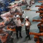 Two Caucasian engineers shaking hands amidst advanced robotics in a high-tech manufacturing setup