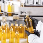 Medical production, pharmacy and healthcare industry. Employee wearing protective clothes holding bottle with golden substance in his hands, conducting quality control of end product at factory