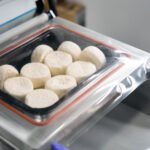 Vacuum packaging of cottage cheese pancakes in the semi-finished products workshop, staff working in protective gloves